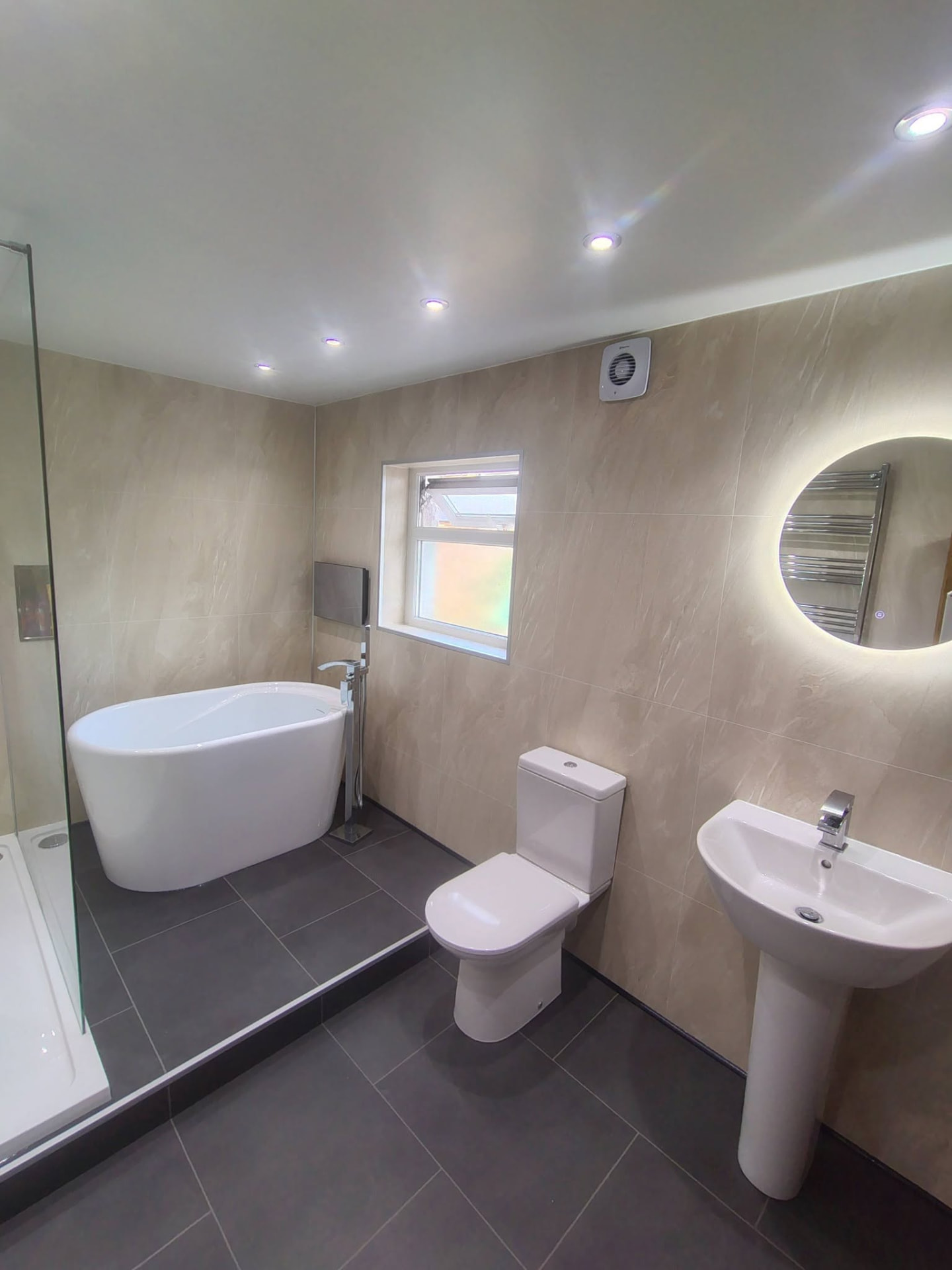 Finished bathroom with freestanding bath and illuminated circular mirror